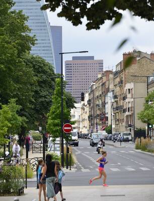 Vue d'une rue à Courbevoie, avec une joggeuse, des immeubles et des arbres